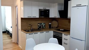 Una cocina moderna con armarios blancos, un microondas, una estufa y un refrigerador. Hay una mesa redonda con cuatro sillas blancas.