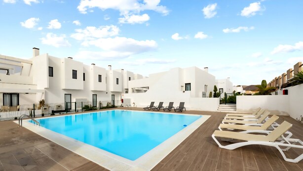 Un área de piscina moderna con una piscina azul cristalina, tumbonas y edificios blancos contemporáneos.