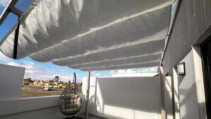 Un balcón con una silla colgante, una mesita y vistas de la ciudad.