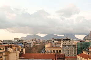 A cityscape with buildings, a street, and mountains in the background. - Ruggero City View Apartment by Wonderful Italy (Palermo)