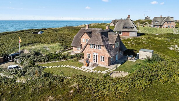 Et kysthus med stråtækt tag, omgivet af en velplejet have og udsigt til havet.