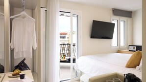 Habitación de hotel con cama, televisión, escritorio con cafetera y vista al balcón.