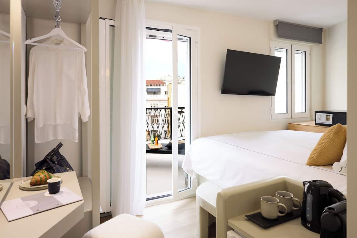 A hotel room with a bed, a TV, a desk with a coffee maker, and a balcony view.