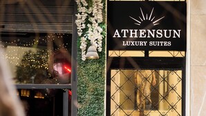 Entrada de un hotel con un letrero que dice 'ATHENSUN LUXURY SUITES'.