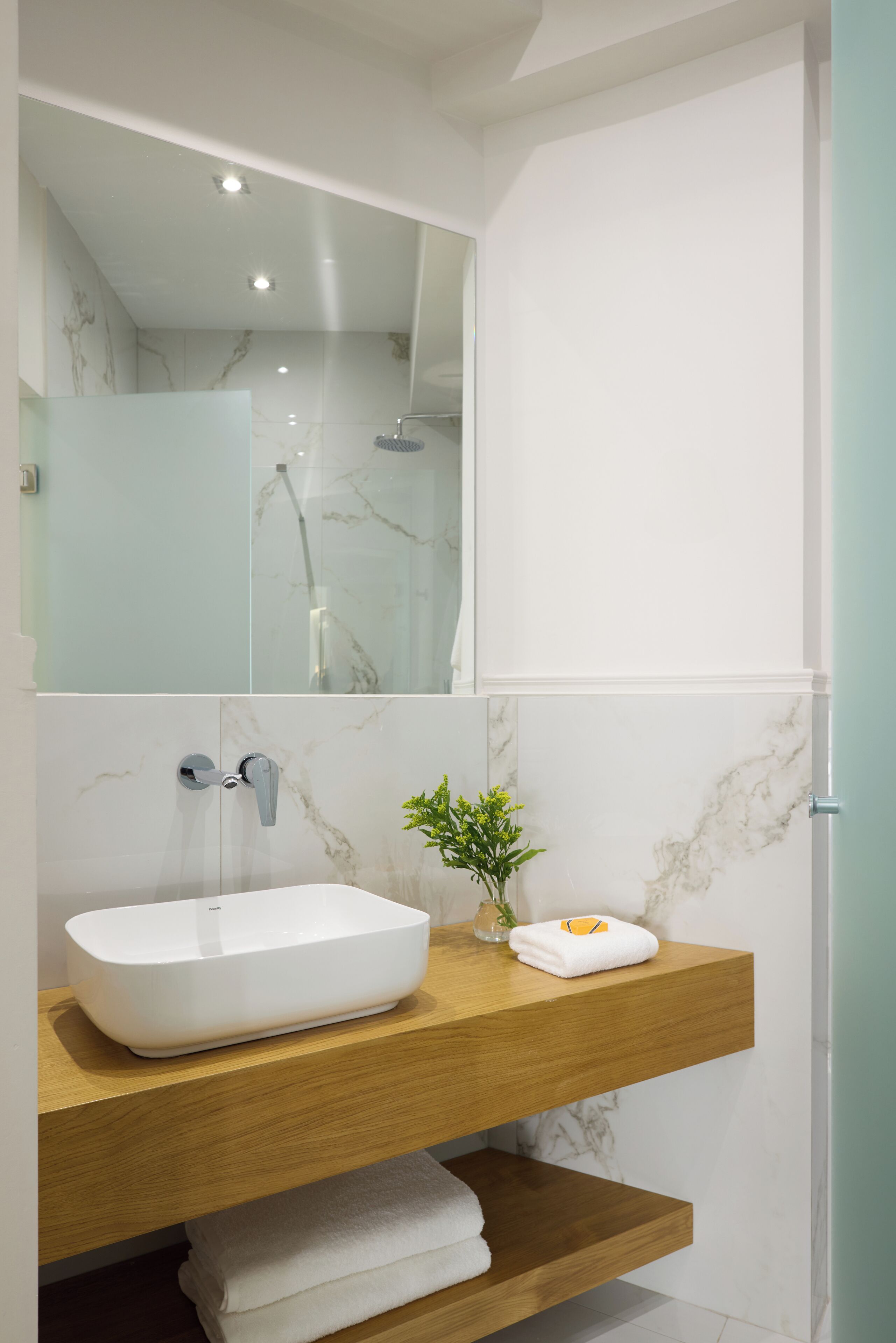 A modern bathroom with a white sink, marble backsplash, and a wooden vanity.
