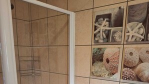 Une salle de bain dotée d’une douche à parois de verre, de toilettes et d’un mur décoré de carreaux sur le thème de la mer.