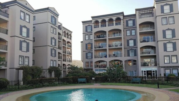 Un immeuble résidentiel doté de nombreux balcons et d’une piscine circulaire entourée d’un chemin pavé en briques.