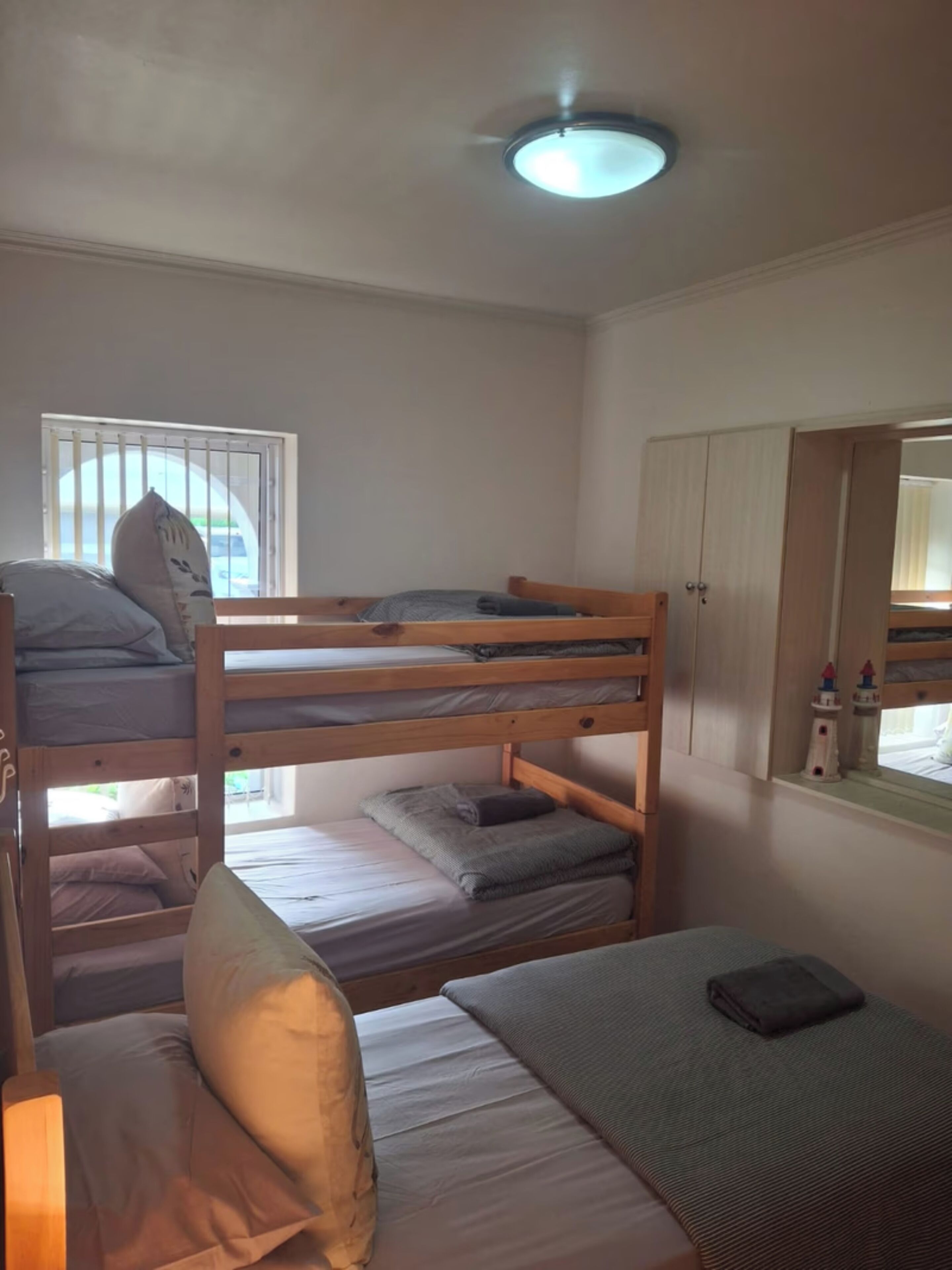 A bunk bed room with a window, a mirror, and a bedside table.