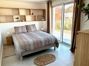 Quarto com cama, mesa de cabeceira, abajur, janela com cortinas e vista exterior.