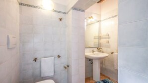 Une salle de bain avec des carreaux blancs, des toilettes, un lavabo et un miroir.