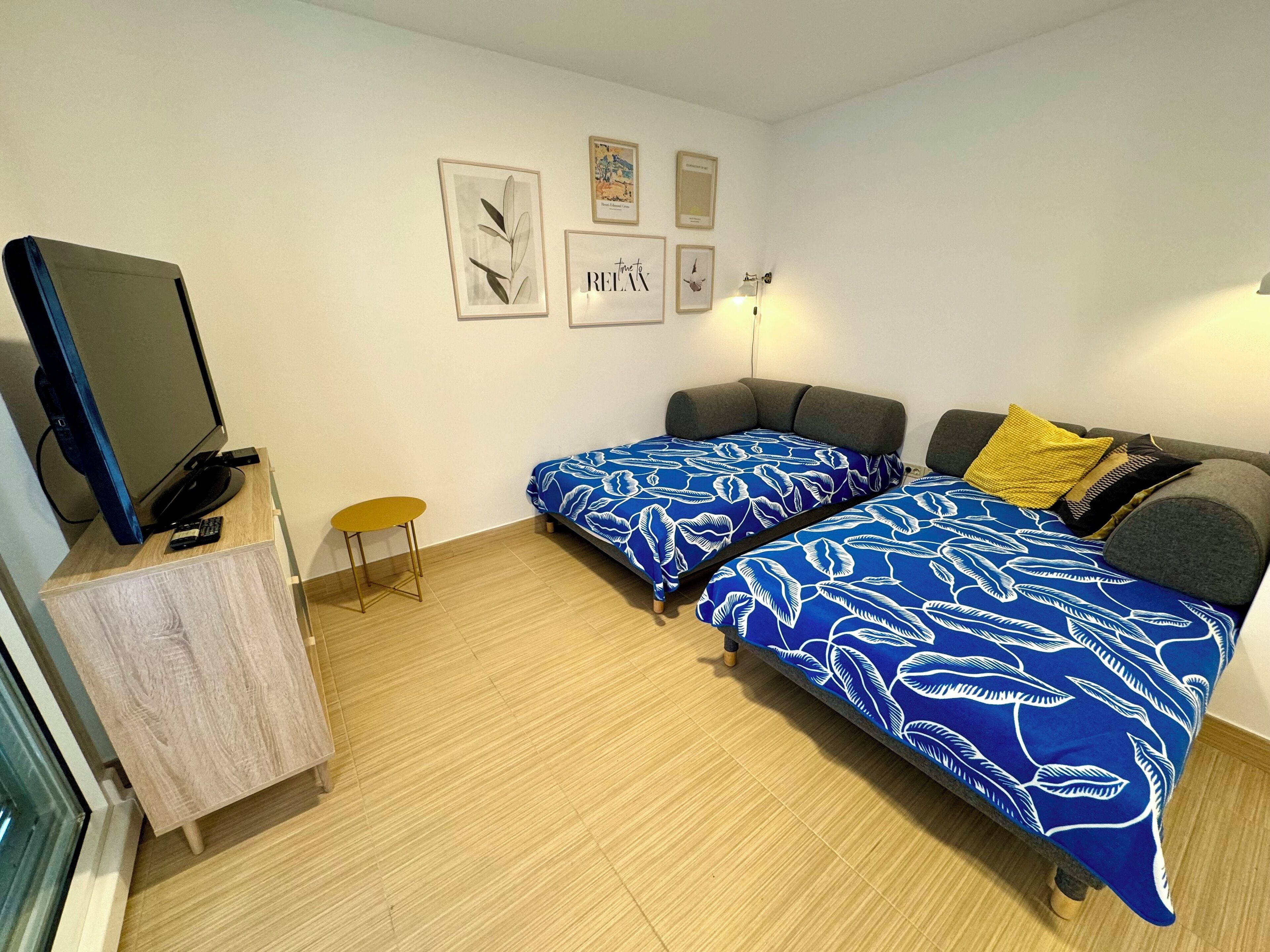 A compact room with two single beds, a small table, a TV on a cabinet, and a wall-mounted lamp.