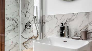Un baño con ducha de mármol, lavamanos blanco y tocador de madera.