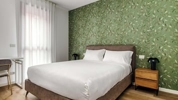 Un dormitorio con cama, mesita de noche, escritorio y ventana con cortinas.