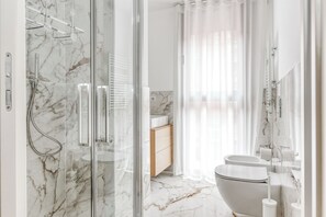 Ein modernes Badezimmer mit Duschkabine aus Glas, Marmorboden, einem Holzwaschtisch und einer Toilette.