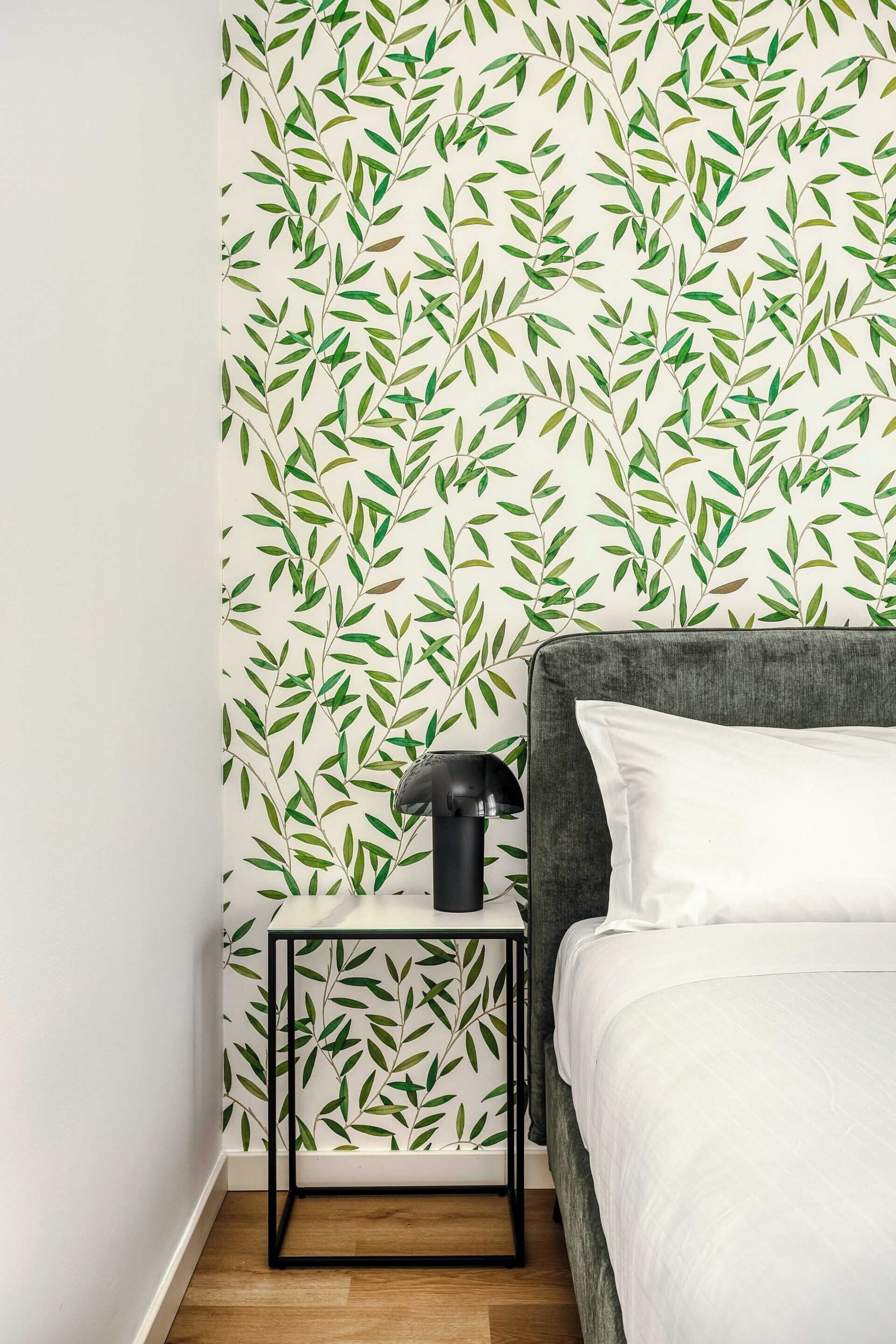 Un dormitorio con una cama, una mesita de noche y un papel tapiz con estampado de hojas.