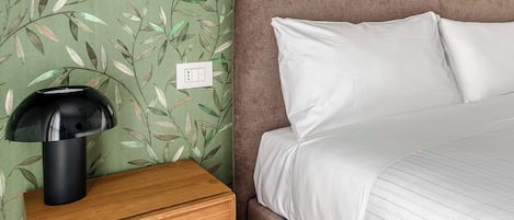 Una cama bien hecha con sábanas blancas, cabecera de madera marrón y una mesita de noche con lámpara.