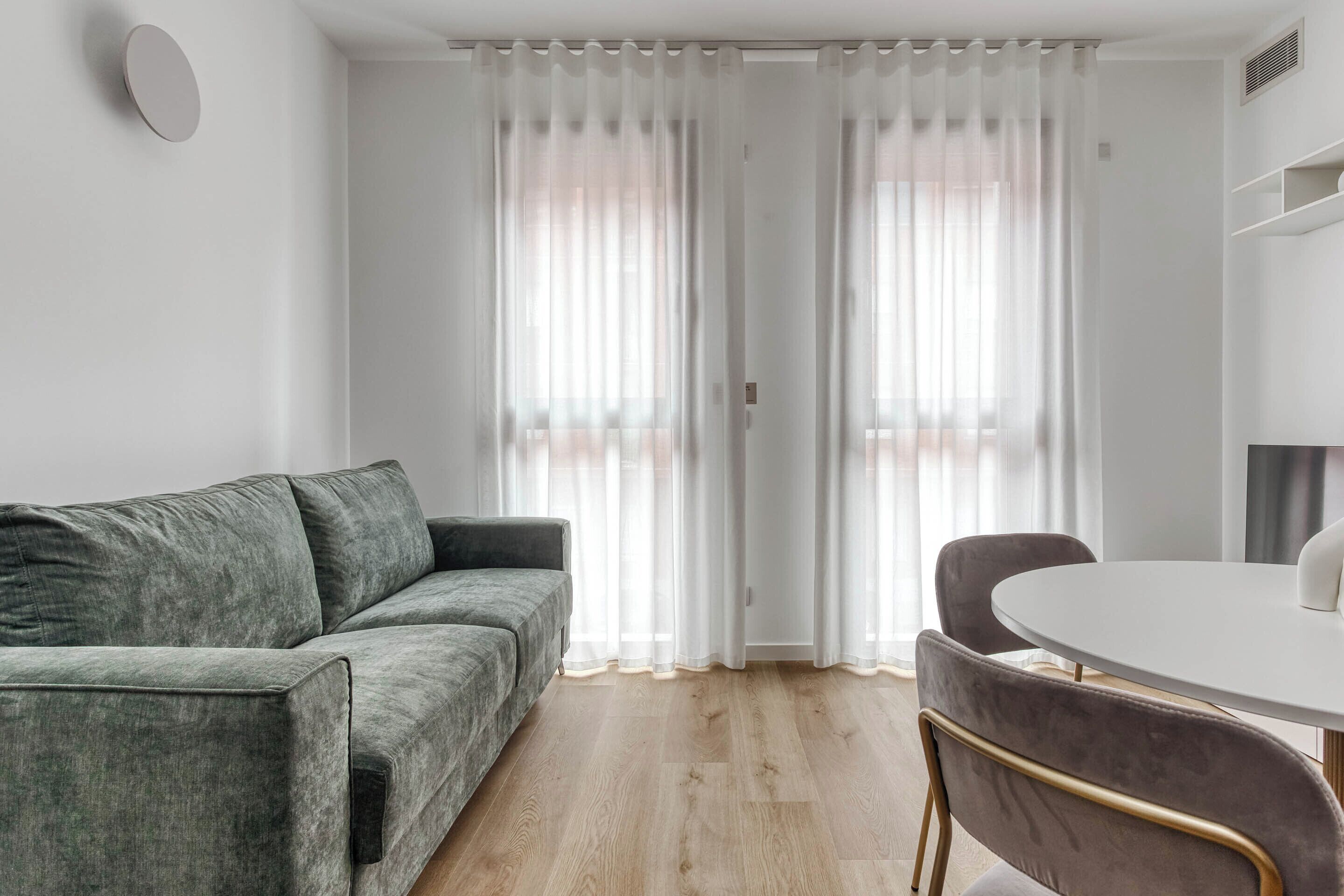 A modern living room with a grey sofa, a round white table, and a dark brown chair.
