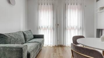 Un salon moderne avec un canapé gris, une table ronde blanche et un fauteuil marron foncé.
