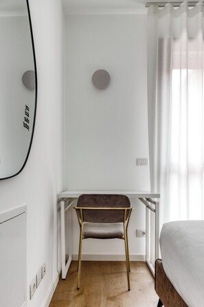 Ein modernes Zimmer mit Holzboden, einem Bett, einem Schreibtisch mit Stuhl, einem Spiegel und einem Fenster mit Vorhängen.