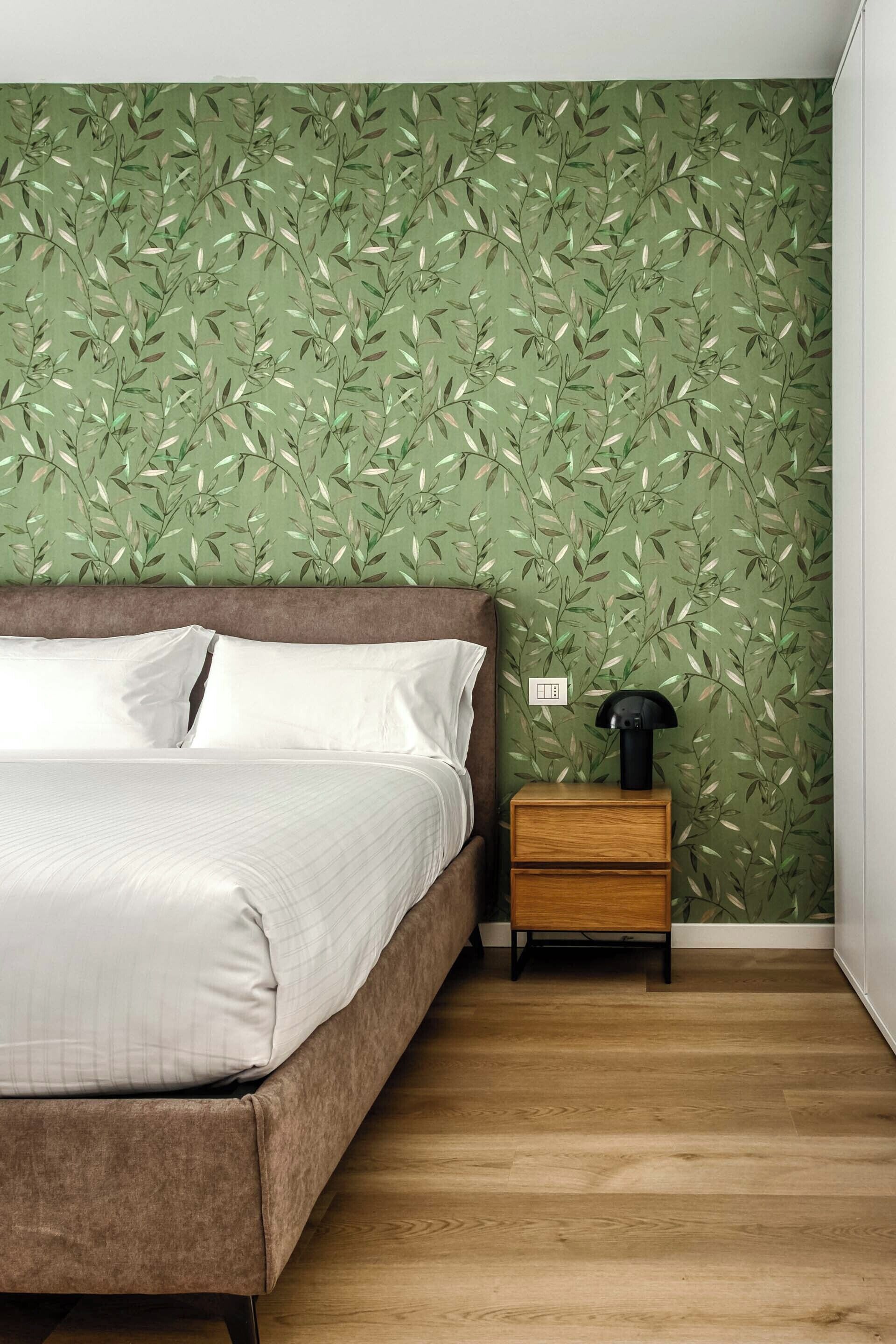 A bedroom with a bed, a nightstand, and a wall with a leafy pattern.