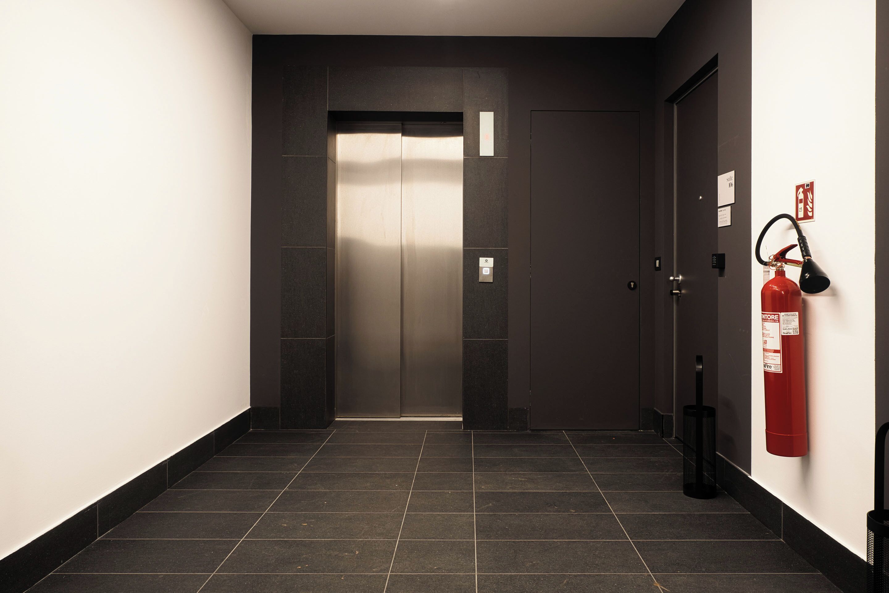 A hallway with a closed elevator door, a fire extinguisher, and a trash bin.