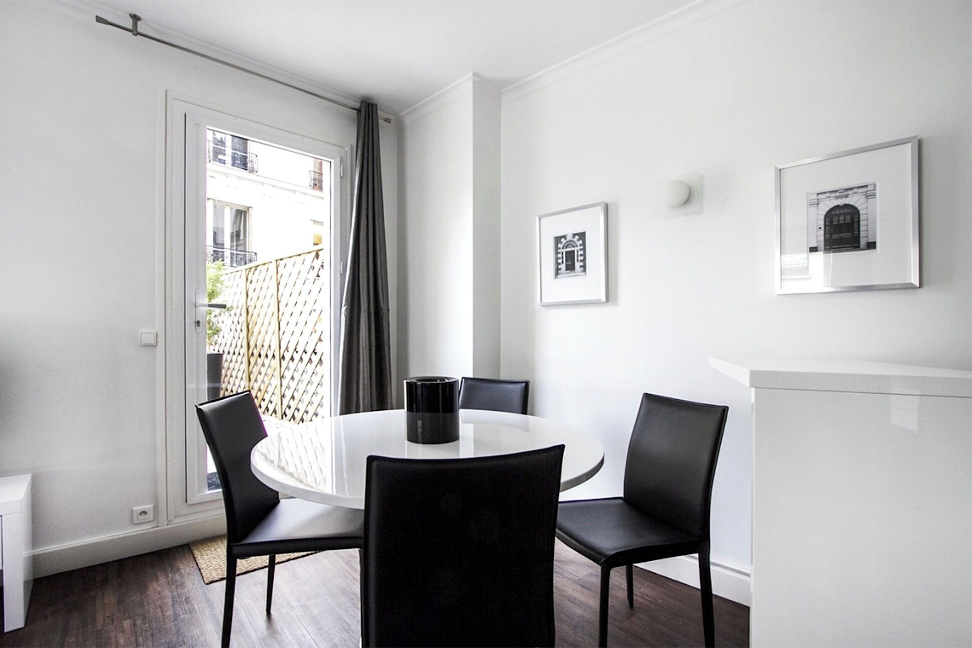 A modern, minimalist room with a round dining table and four chairs, a white radiator, and two framed pictures on the wall.