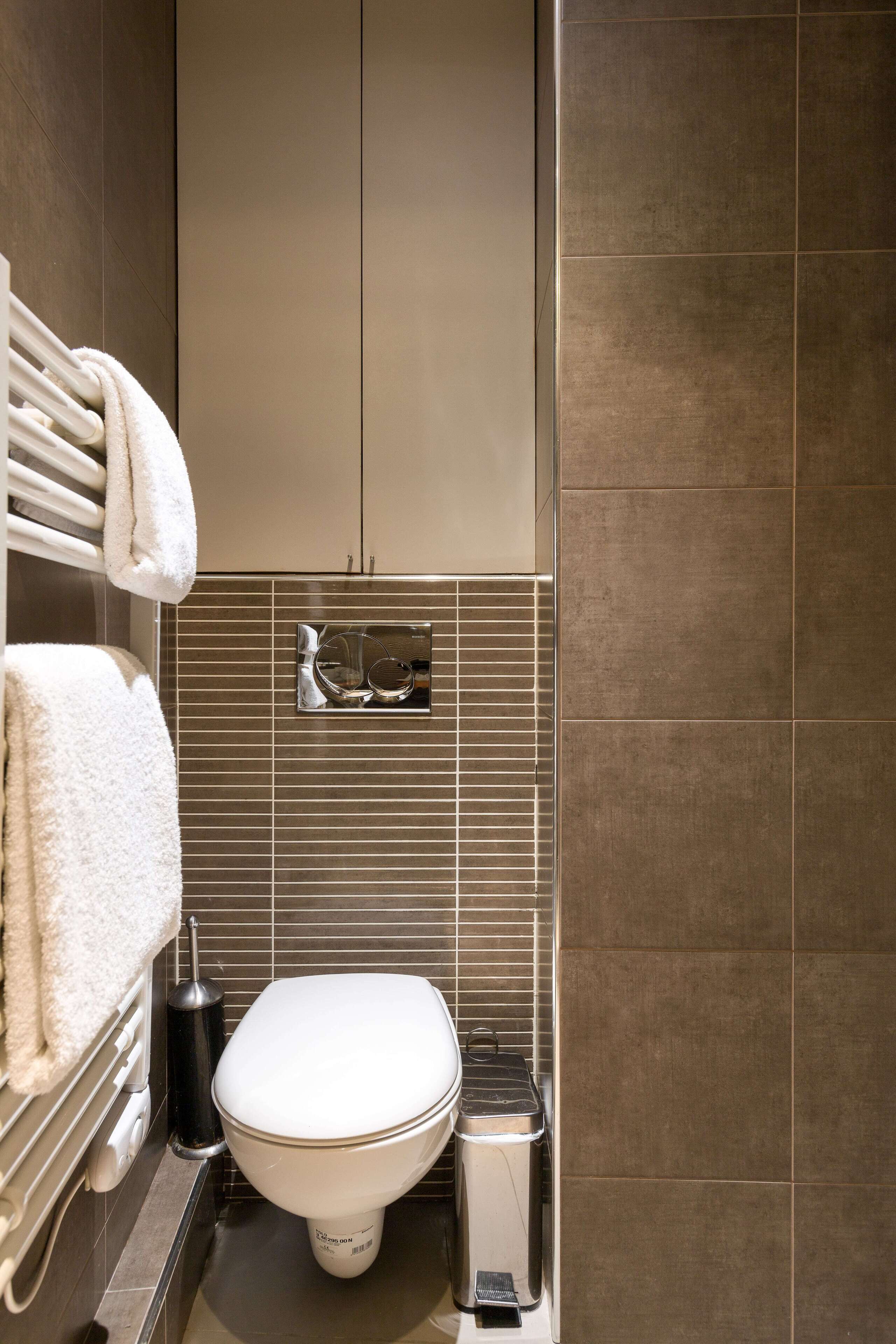 A modern bathroom with a toilet, a towel rack, and a trash bin.