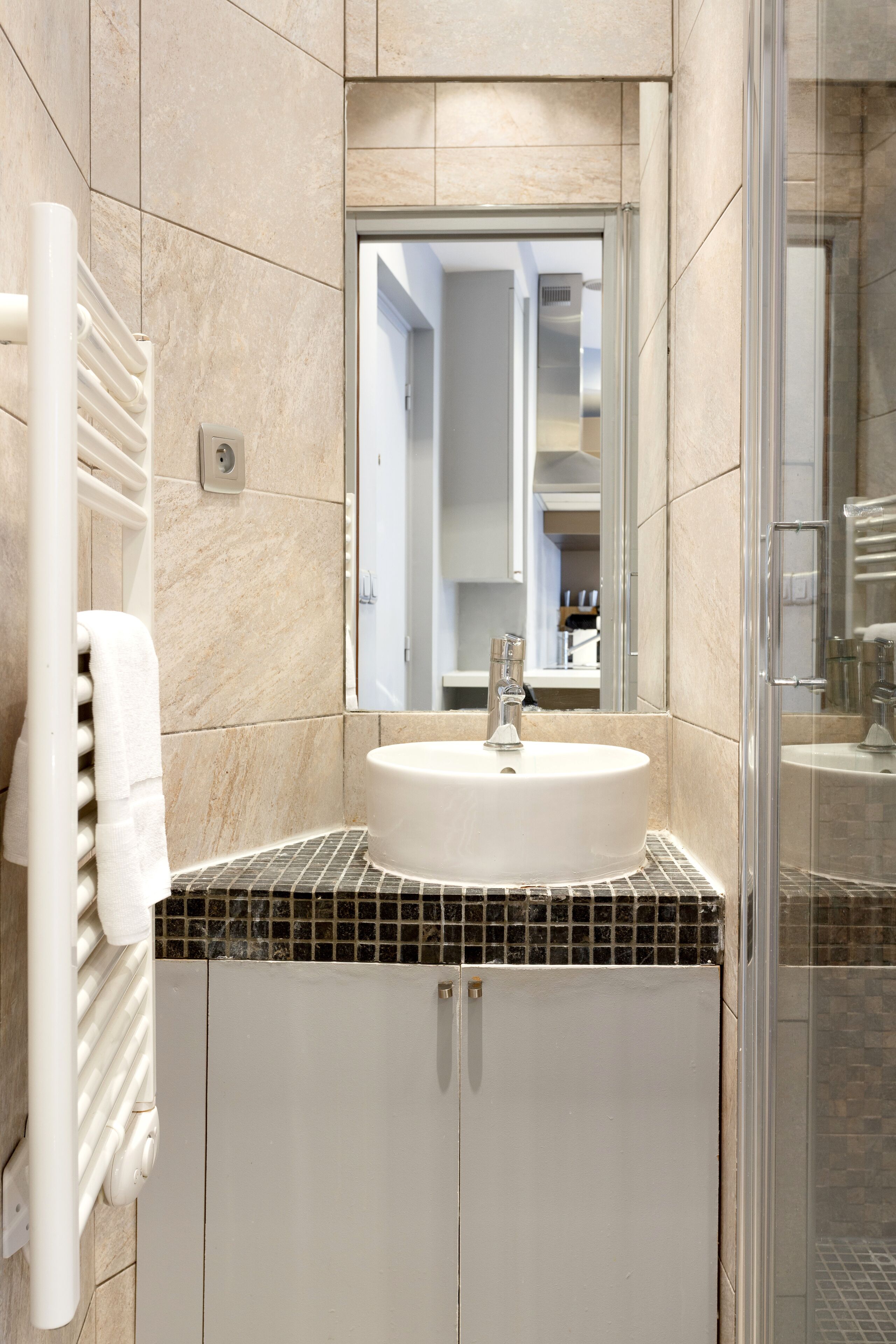 Un baño con lavamanos blanco, un espejo y una cabina de ducha de vidrio.