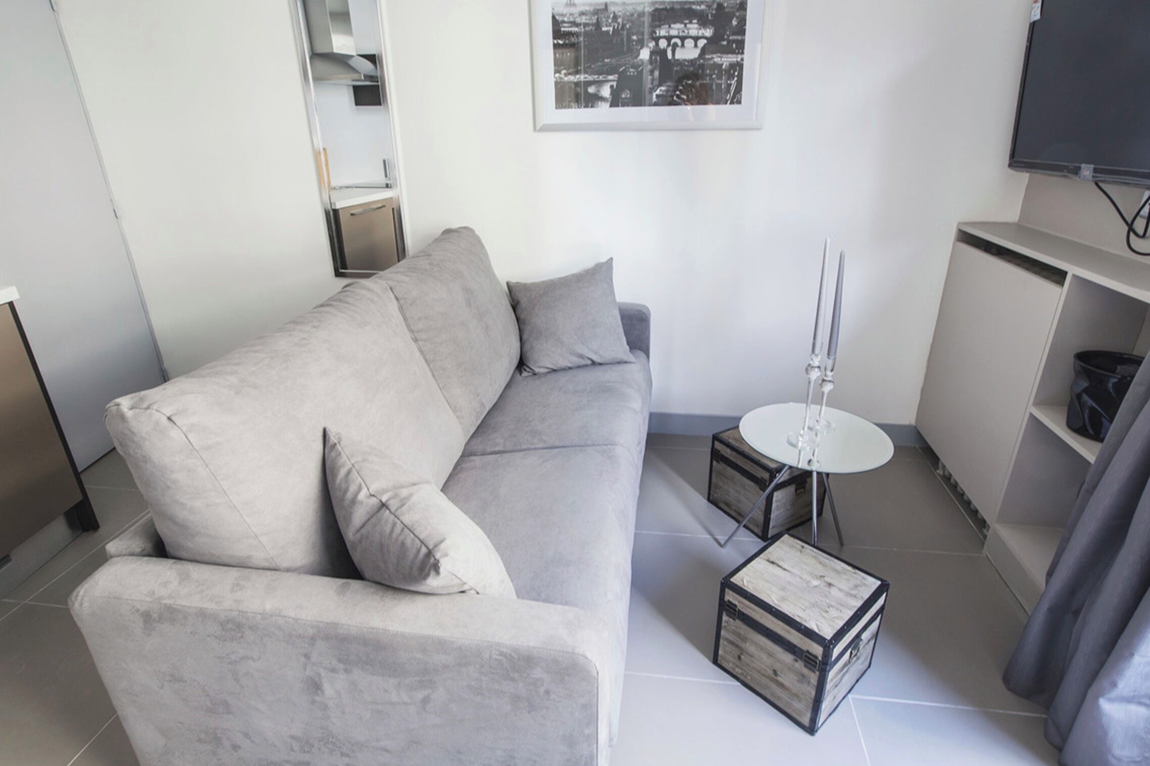 A modern living room with a grey sofa, a small round table, and a television mounted on the wall.