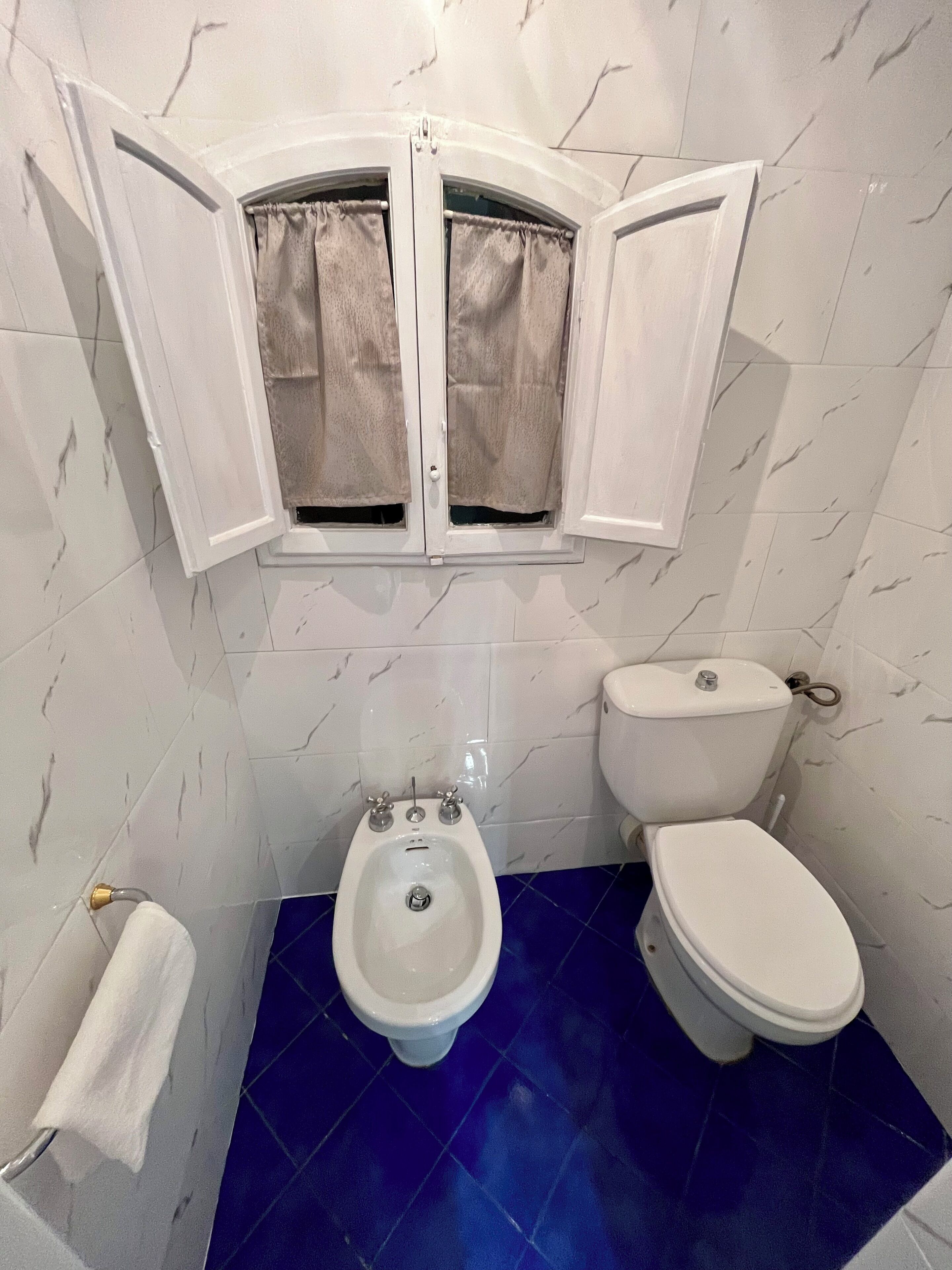 A bathroom with a bidet, toilet, and a window with curtains.