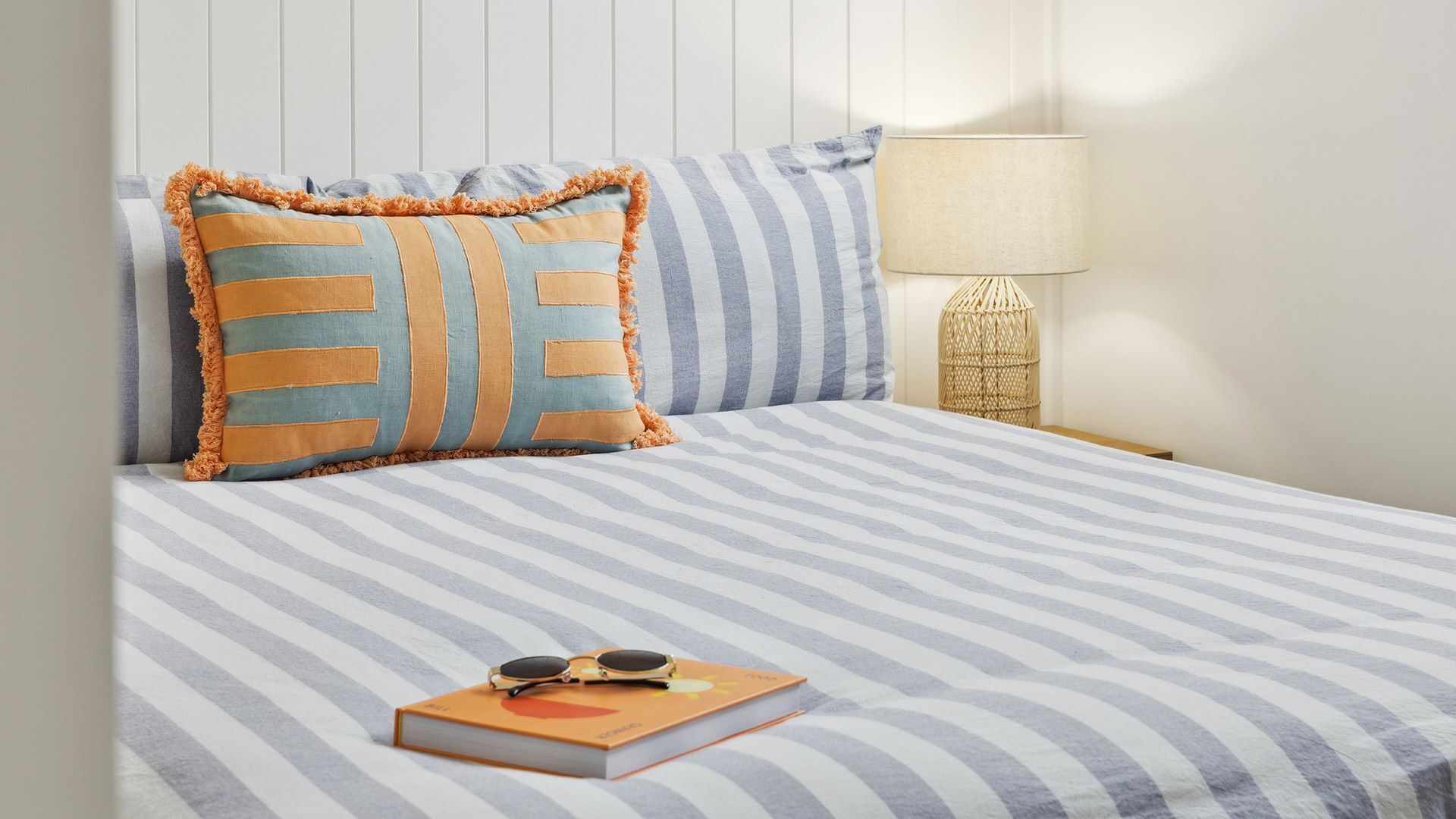 Un lit avec une literie à rayures, un oreiller à motifs rayés, un livre et une paire de lunettes de soleil posées sur le lit.