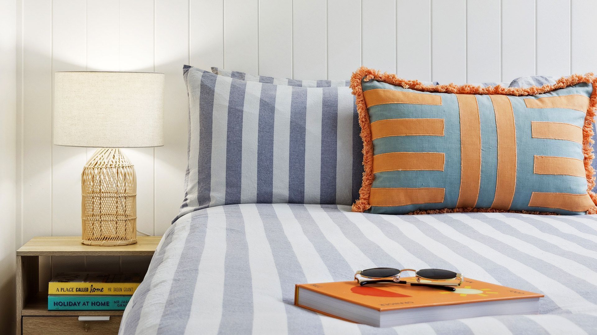 A neatly made bed with striped bedding, a bedside lamp, and books on a nightstand.