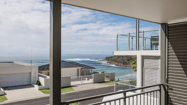A residential property with a balcony overlooking a coastal view, a garage, and a modern architectural design.