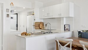 Une cuisine moderne avec des meubles blancs, un îlot central doté d’un évier et une table à manger en bois.