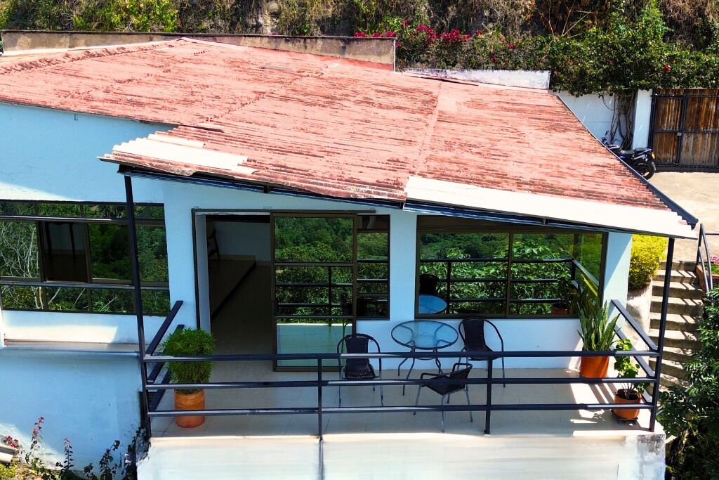 Una casa moderna con techo inclinado, ventanas grandes y un balcón con mobiliario exterior.