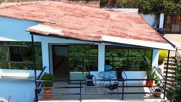 Una casa moderna con techo inclinado, ventanas grandes y un balcón con mobiliario exterior.
