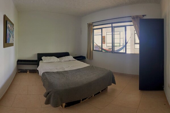 A bedroom with a bed, a window with curtains, a desk, and a wardrobe.