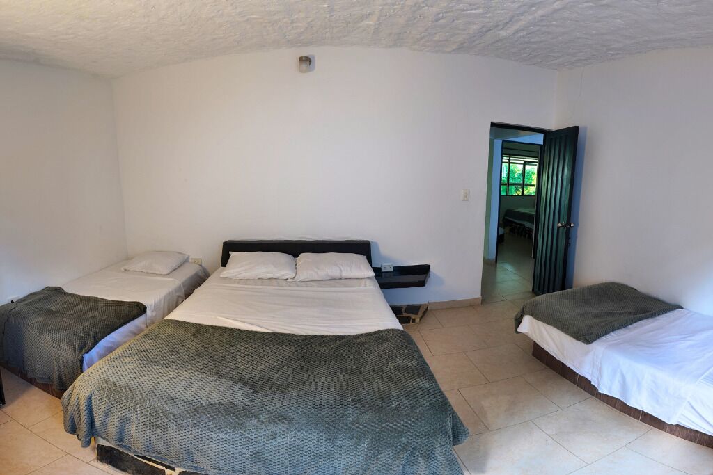A room with three beds, a small window, and a door leading to another room.