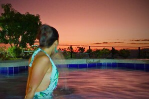 A person standing by a pool with a sunset in the background.