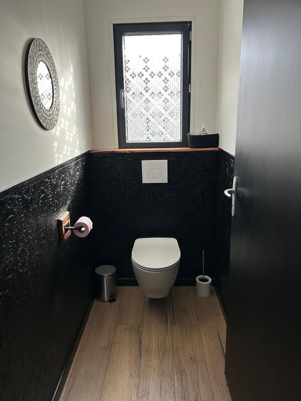 Un baño compacto con inodoro, secamanos, cubo de basura y ventana con vidrio decorativo.