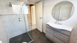 Une salle de bain dotée d’une douche à parois de verre, d’un miroir rond et d’un lavabo blanc avec un meuble-vasque en bois.