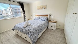 Une chambre à coucher avec un lit, des tables de chevet, une commode, un tableau et une fenêtre avec des stores.