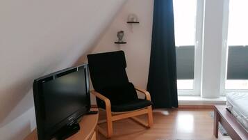 Ein Zimmer mit einem Flachbildfernseher auf einem Holzständer, einem schwarzen gepolsterten Sessel, einer Holzbank und einem grauen Teppich.