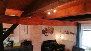 Zona d'estar acollidora amb sostre de fusta, un sofà de cuir negre, una taula de centre i una cuina amb microones i cafetera.