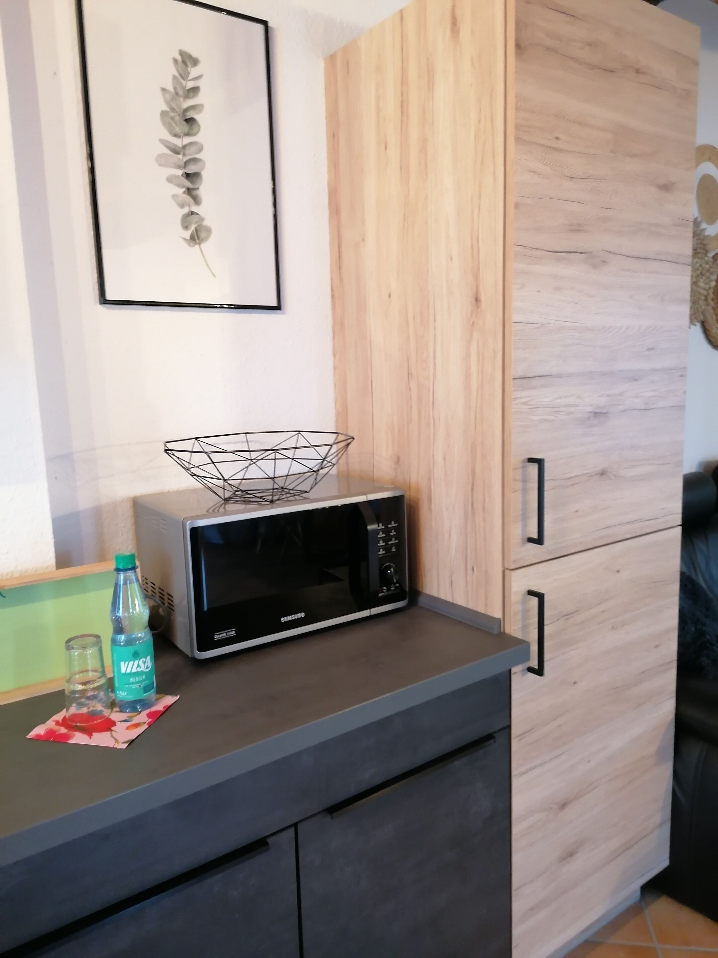Un coin cuisine avec un four à micro-ondes posé sur un plan de travail, une bouteille d’eau et un petit verre.