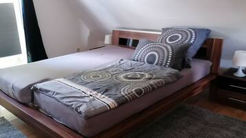 Una cama individual con un edredón estampado y almohadas, una mesita de noche con una lámpara, y una ventana con cortinas.