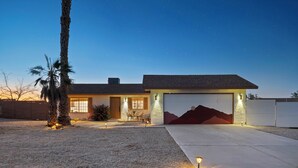 A modern house with a garage, a gravel driveway, and a palm tree. - Desert escape w/ hot tub, pool, fire pit & fully fenced yard — 15 min to JTNP. Perfect for dog-friendly getaways. 🌵✨ (Joshua Tree)