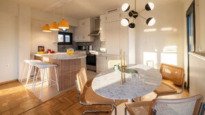 A modern kitchen with white cabinets, a round marble island, and a dining area with wicker chairs. - Athens Panorama Penthouse by the Acropolis (Athina)
