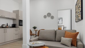 A modern living room with a grey sofa, a small round table, and a kitchen area with cabinets and appliances. - Forth House by Supercity Aparthotels (Edinburgh)