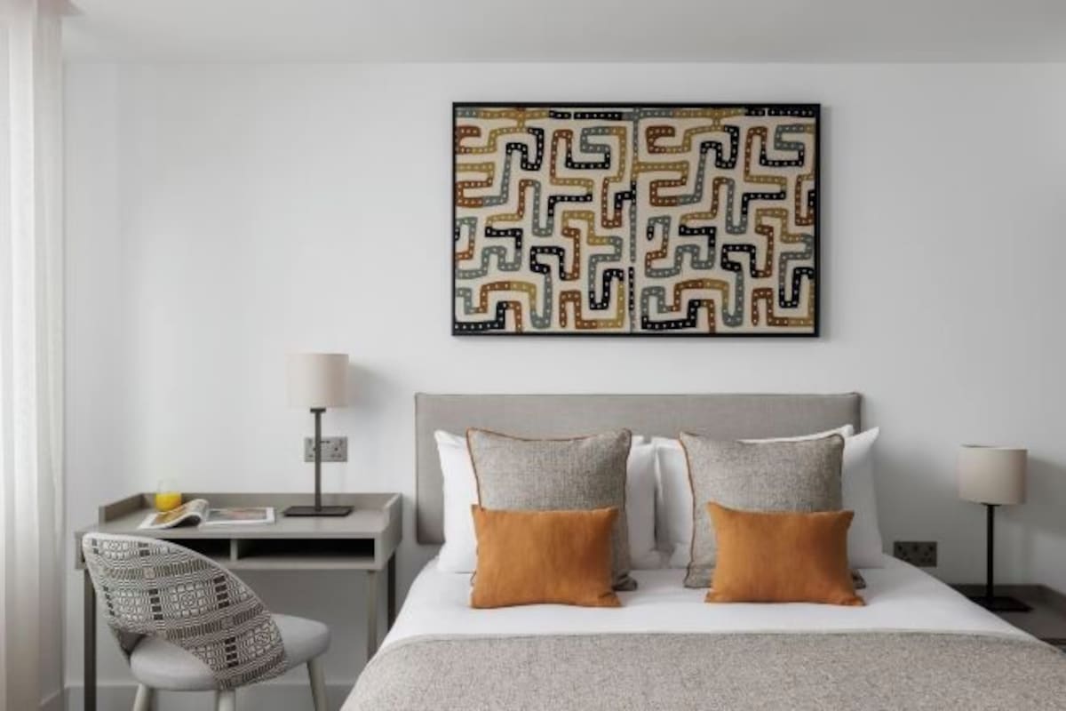 A neatly arranged hotel room with a bed, bedside tables, a chair, and a wall-mounted artwork.
